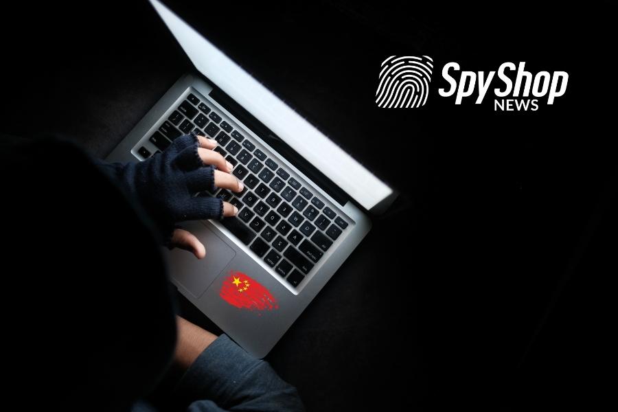 Mężczyzna w kapturze pisze coś na klawiaturze laptopa, na którym jest chińska flaga.