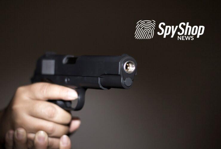 Mężczyzna trzyma w dłoni wycelowany pistolet. Tło jest czarne