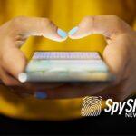 Zbliżenie na dłonie kobiety z pomalowanymi paznokciami, w których mieści się telefon z włączonym komunikatorem typu WhatsApp